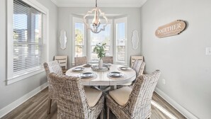 Uma sala de jantar com uma mesa redonda, cadeiras de vime, um candelabro e um letreiro na parede com a palavra 'TOGETHER'.