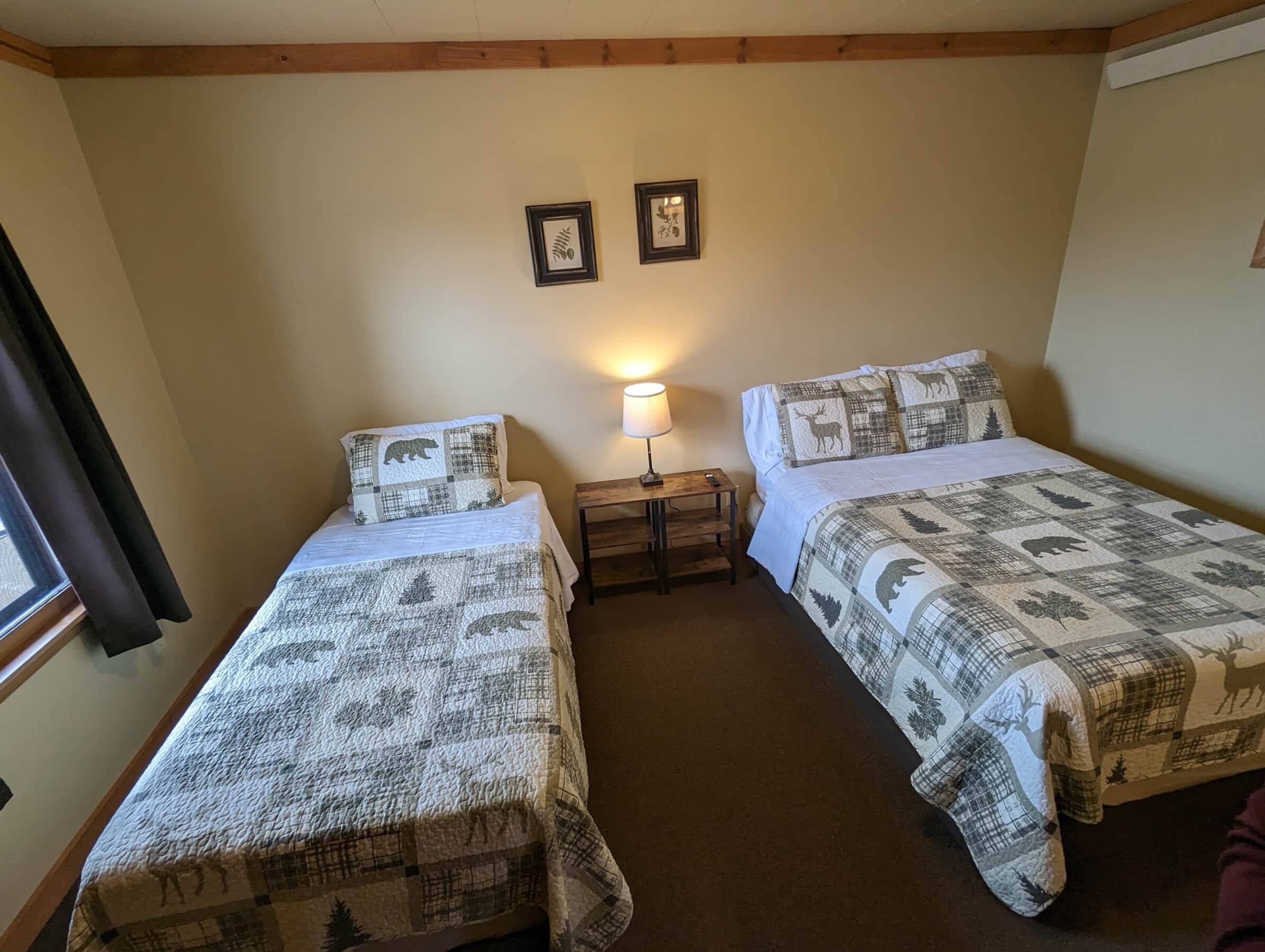 Une chambre avec deux lits, chacun recouvert d’une courtepointe matelassée ornée de motifs animaliers. Deux tableaux encadrés sont accrochés au mur, au-dessus des lits.