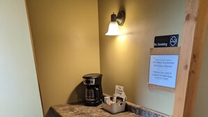 Une petite cuisine équipée d’une machine à café, d’un petit tabouret de bar, d’une lampe fixée au mur et d’un panneau indiquant qu’il est interdit de fumer.