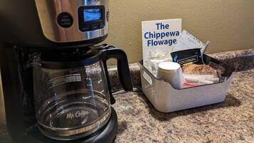 A Mr. Coffee coffee maker on a granite countertop next to a basket labeled "The Chippewa Flowage" containing a coffee pod and a white mug.