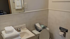 Une salle de bain avec un lavabo, des toilettes et un miroir. Des serviettes sont pliées sur le lavabo et une poubelle se trouve à côté des toilettes.