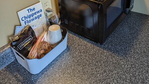 A coffee maker on a countertop with a sign reading "The Chippewa Flowage" and a basket containing coffee pods and a mug. - Chip-Wa Lodging Room 5 (Hunter)