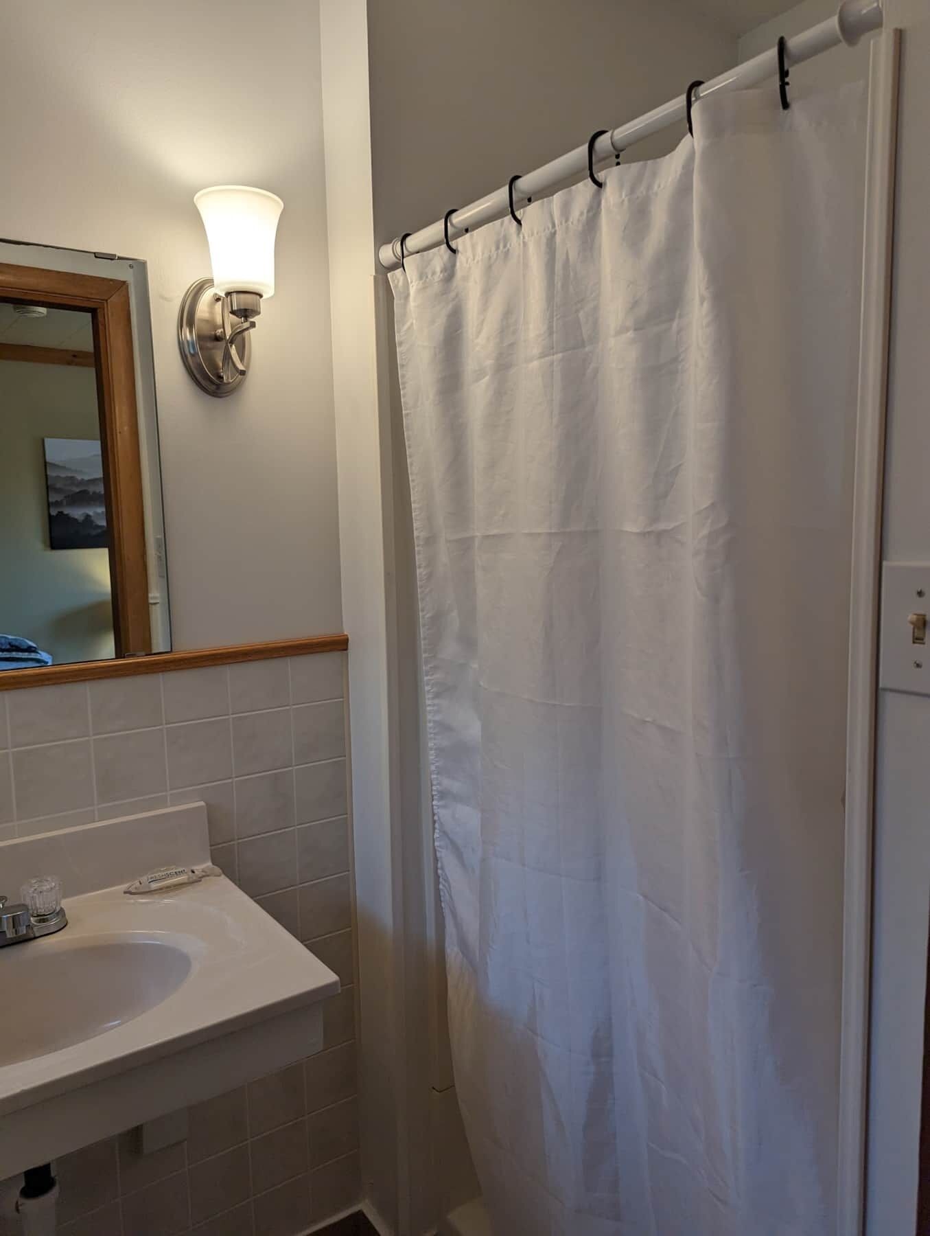 Un baño con lavamanos blanco, espejo y cortina de ducha.