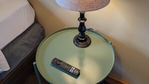 A round glass table with a remote control and a lamp with a textured lampshade. - Chip-Wa Lodging Room 5 (Hunter)