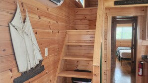 Puinen mökki, jonka sisätiloissa on sisäänrakennettu ilmastointilaite, pienet portaat ja sänky viereisessä huoneessa.