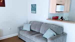 A living room with a grey sofa, a wooden cabinet, and a microwave. - Perfectly Located Studio in MB (Myrtle Beach)