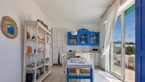 A kitchen with white and blue cabinetry, a dining table with chairs, and a view through a sliding glass door to an outdoor patio.