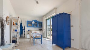 A compact room with a dining table, a blue wardrobe, and a white cabinet with glass doors.