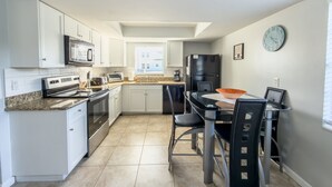 A modern kitchen with white cabinets, a black refrigerator, and a dining area with a glass table and chairs. - Relaxing Apartment Close to the Beach ! (Cape Canaveral)