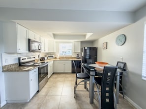 A modern kitchen with white cabinets, a black refrigerator, and a dining area with a glass table and chairs.