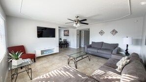 A modern living room with a grey sofa, a red chair, a glass coffee table, and a flat-screen TV mounted on the wall. - Relaxing Apartment Close to the Beach ! (Cape Canaveral)