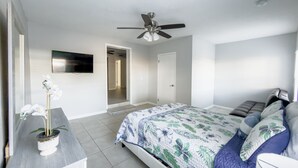 A bedroom with a bed, a ceiling fan, a TV mounted on the wall, and a potted orchid on a nightstand. - Relaxing Apartment Close to the Beach ! (Cape Canaveral)