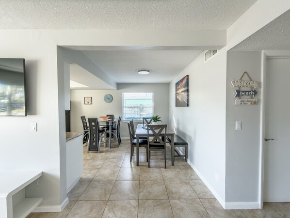 A modern kitchen with a dining area, featuring a large window, a clock, and a welcome sign.