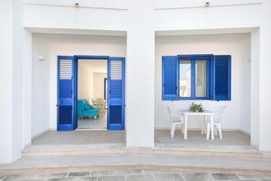 Un edificio con dos puertas abiertas que dan a una habitación con una ventana con persiana azul y una mesa con sillas.