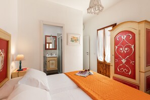 Camera d'albergo con un letto, un comodino con una lampada, una cassettiera e una porta che dà accesso al bagno.