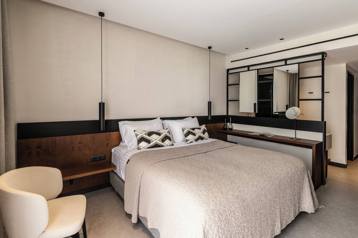 A modern bedroom with a bed, bedside table, chair, and a large mirror.