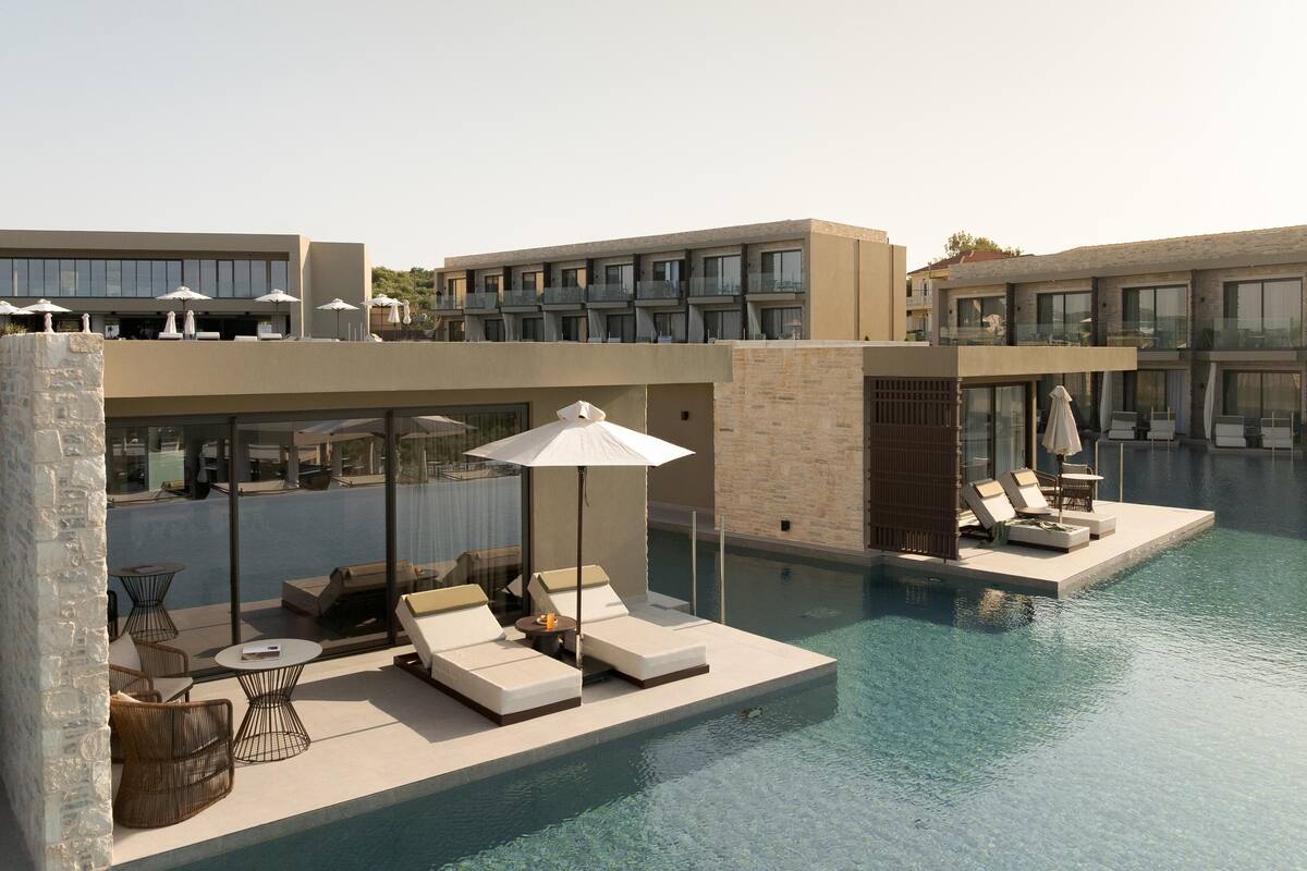 A modern hotel with a rooftop infinity pool, lounge areas with sunbeds and umbrellas, and a view of the surrounding landscape.