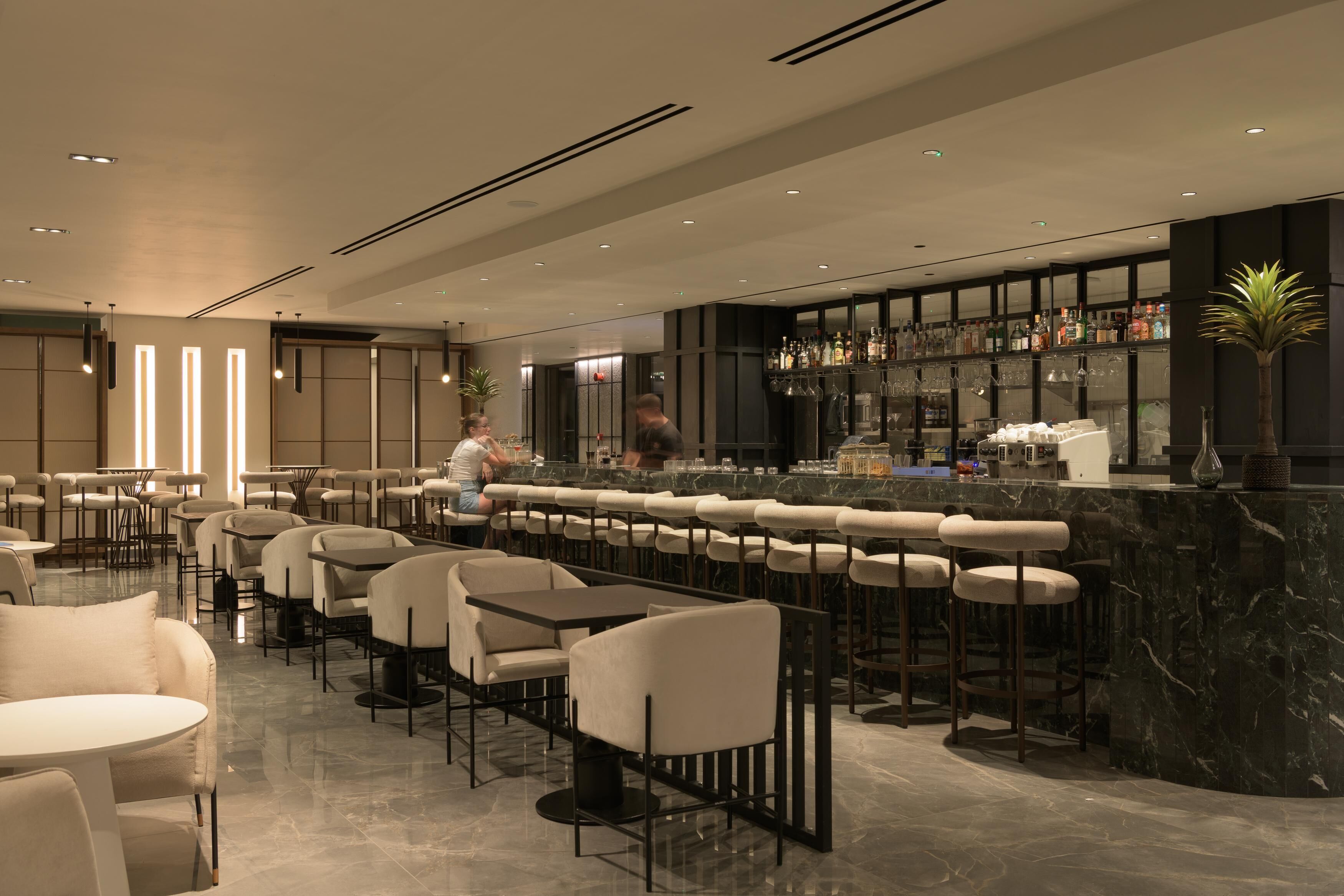 Un espace bar moderne doté d’un long comptoir, de tabourets de bar et d’un bar bien approvisionné.