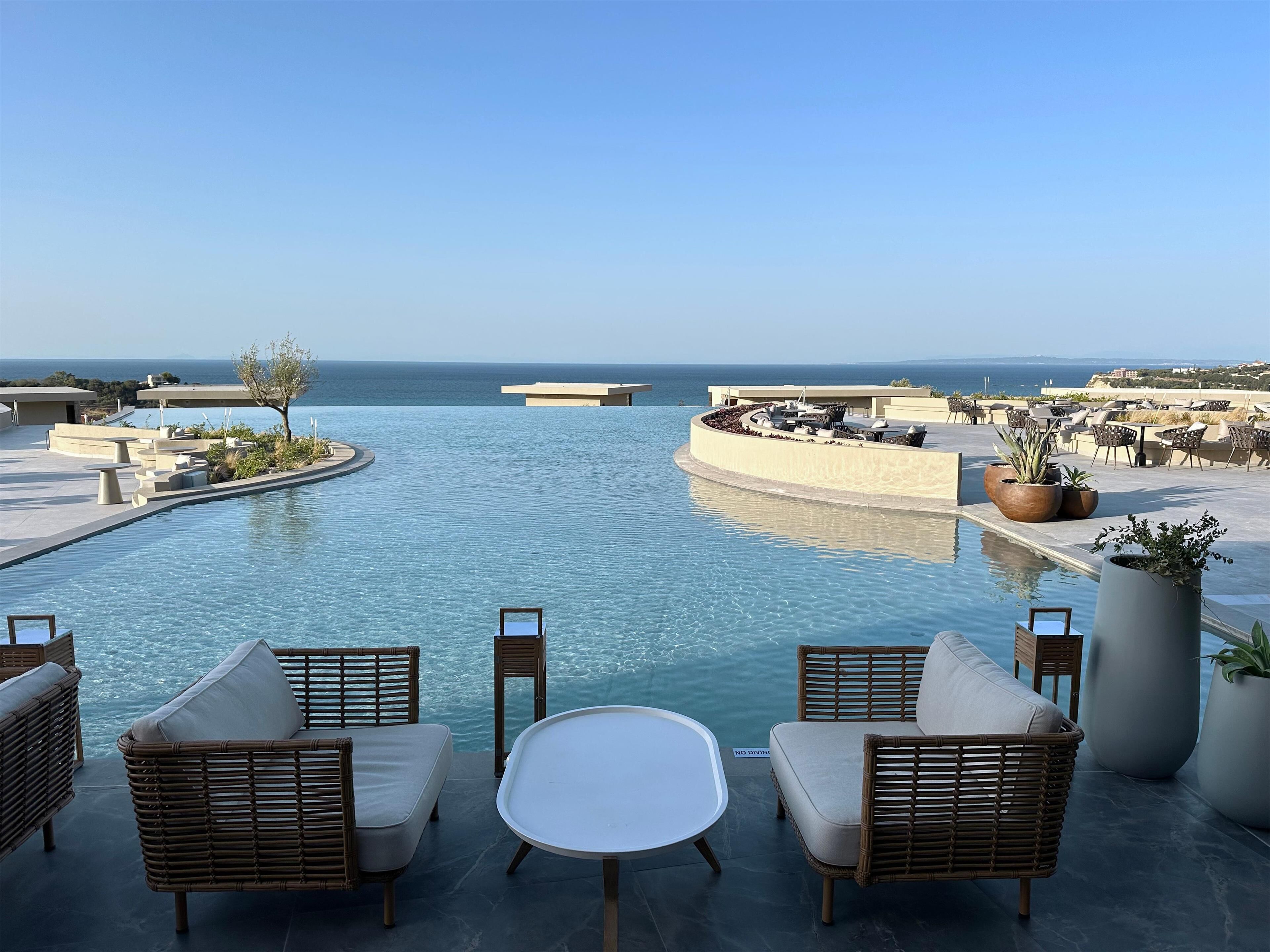 Un espace aménagé au bord de la piscine, avec des meubles en osier, des plantes en pot et une vue sur la mer.