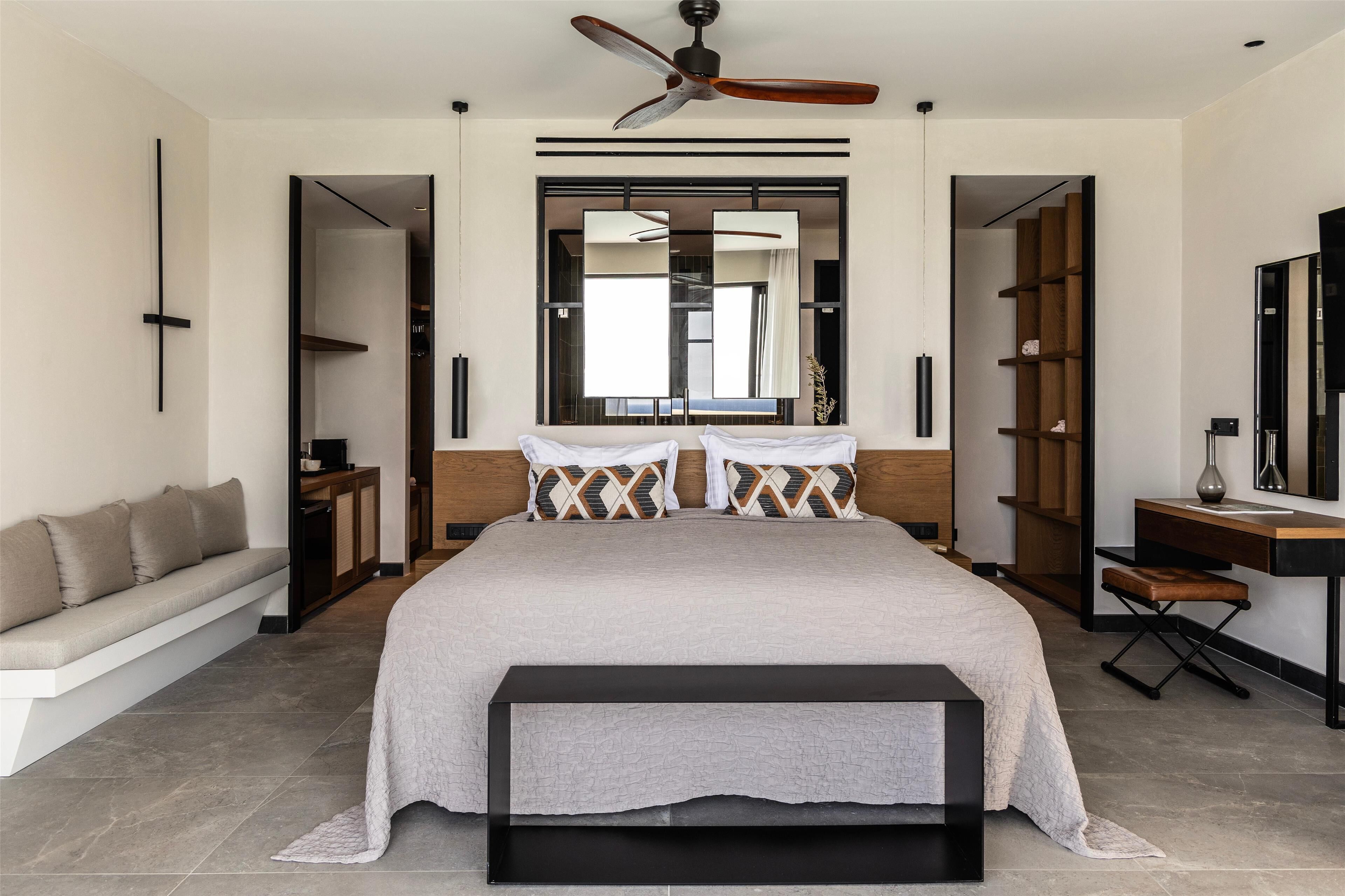 A modern bedroom with a large bed, a ceiling fan, a desk, and a bench.