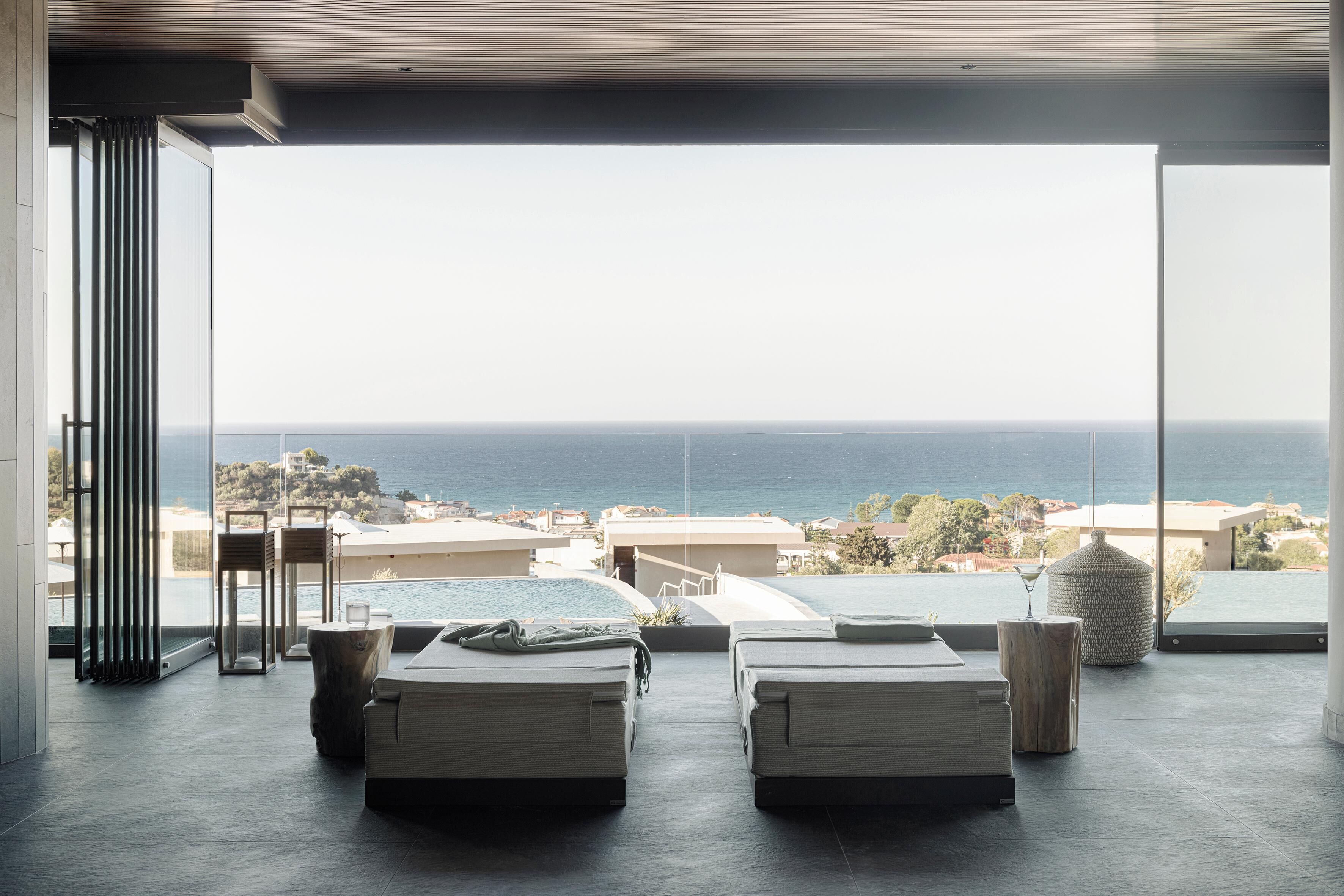 A modern room with two beds, a view of the sea, and a large window.