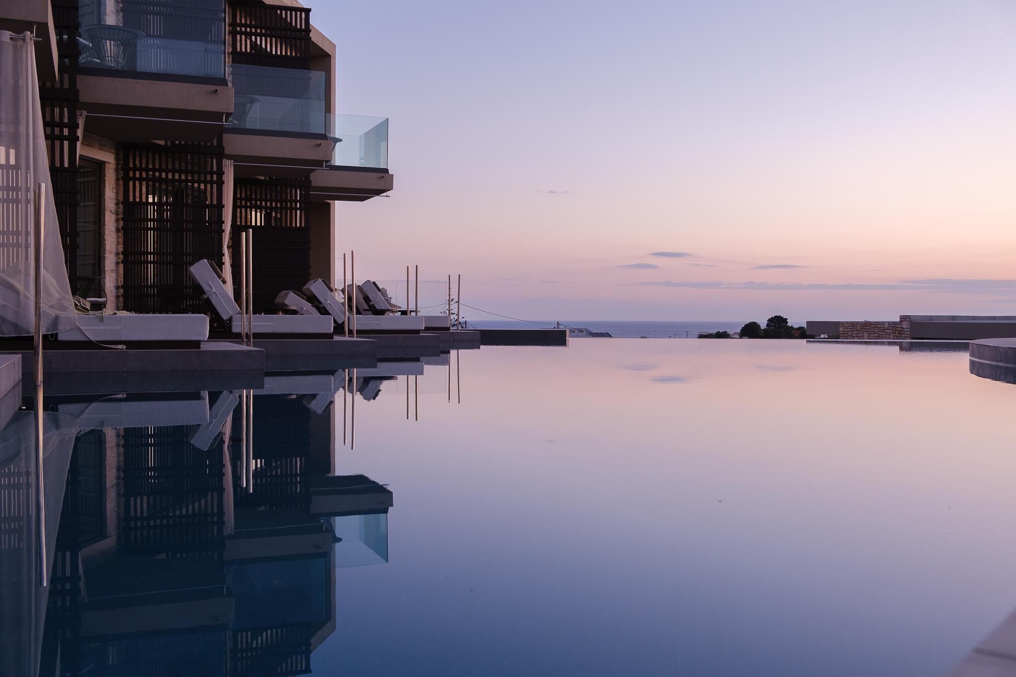 Et moderne hotel med en pool, der spejler bygningen og himlen.