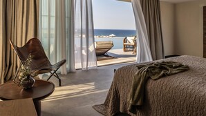 Une chambre d’hôtel avec un grand lit, une chaise, une petite table et une vue sur la mer.