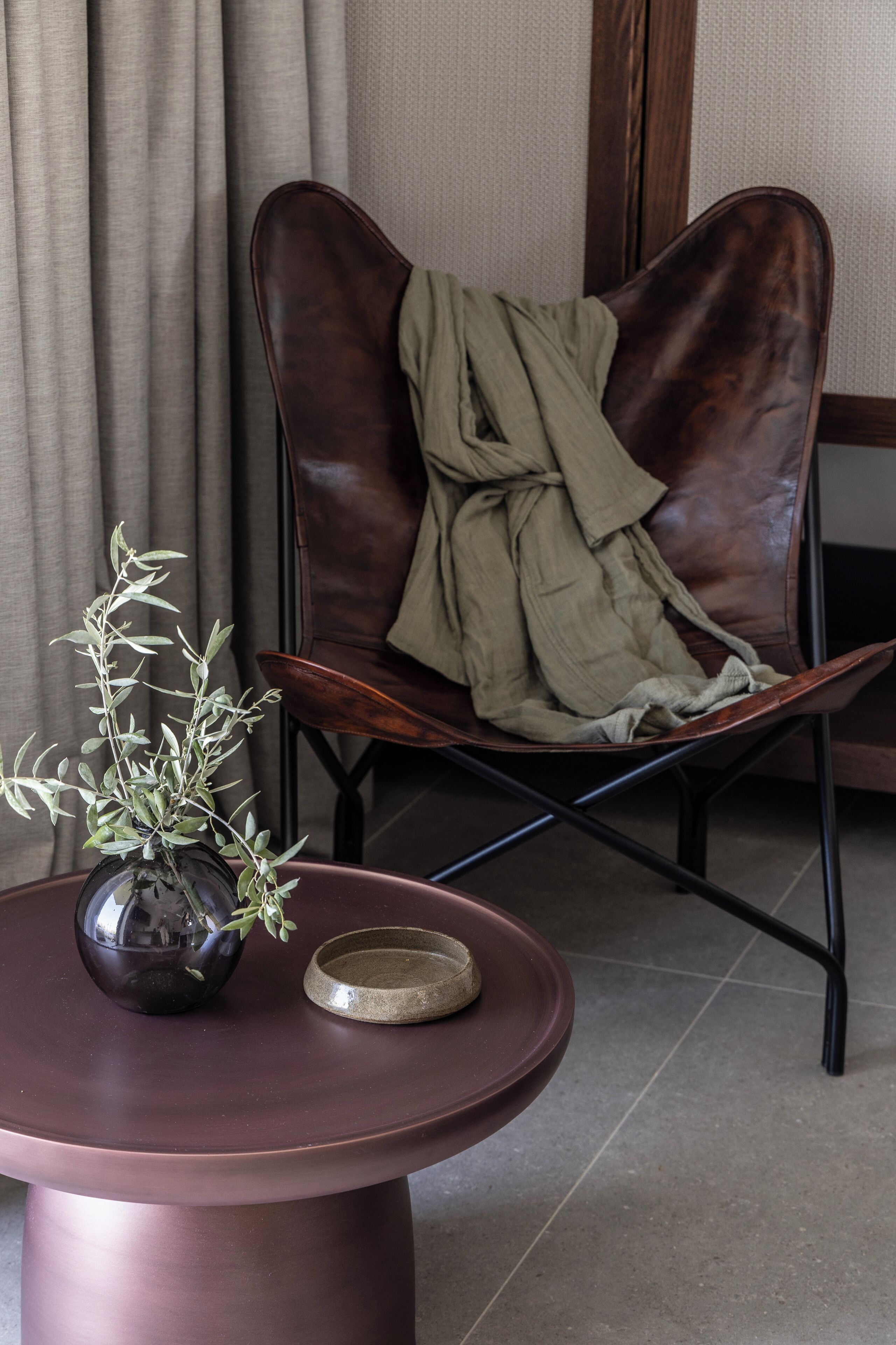 A room with a round table, a brown leather chair with a green cloth, and a potted plant.