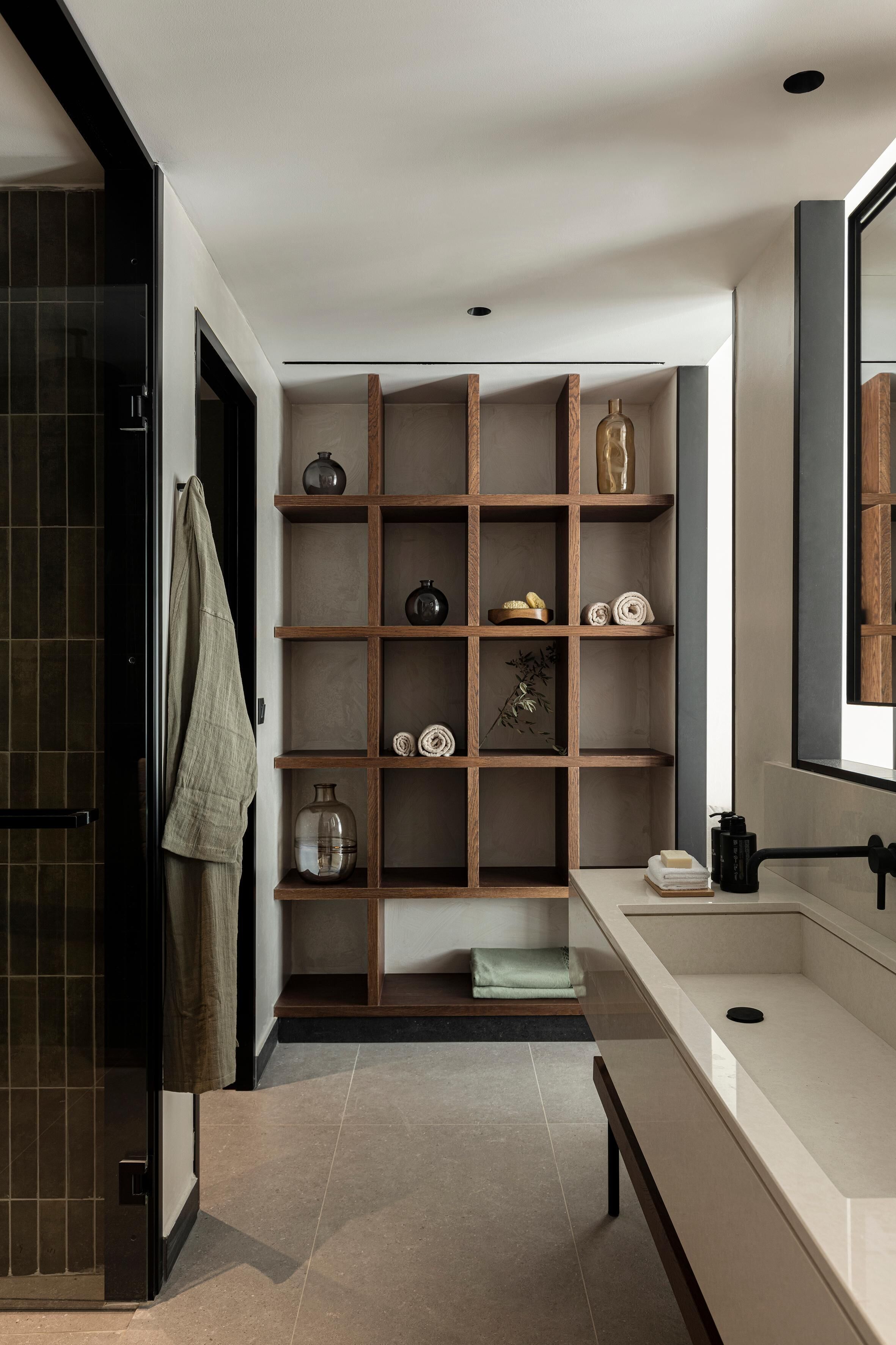 A modern bathroom with a built-in shelf unit, a large mirror, and a countertop with a sink.