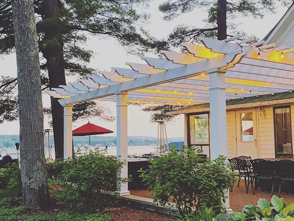 A covered outdoor seating area with a pergola, a red umbrella, and a view of the landscape. - Walk to Walloon Village, Beach & 10 min to Petoskey or Boyne Mountain (Walloon Lake)