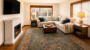 Una sala de estar con chimenea, un sofá modular, una mesa de centro y un televisor montado en la pared.