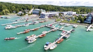 An aerial view of a marina with numerous boats docked at piers, surrounded by residential buildings and a forested area. - Walk to Walloon Village, Beach & 10 min to Petoskey or Boyne Mountain (Walloon Lake)