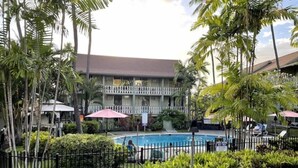 Hotel com piscina rodeada por palmeiras e área cercada.