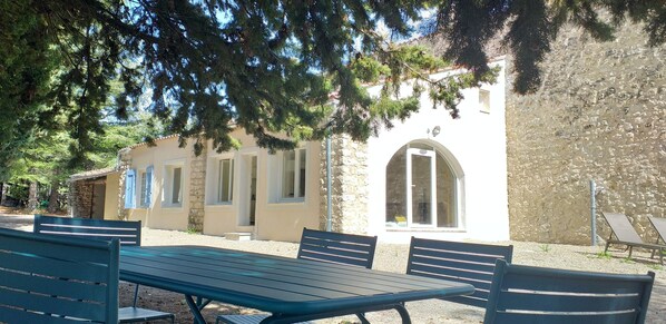 Un espace extérieur aménagé avec une table et des bancs, un mur en pierre et un bâtiment doté de fenêtres en arc de cercle et d’une porte.