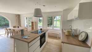 A modern kitchen with a central island, wooden dining table, and large windows.