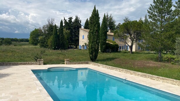 A swimming pool with a stone border, surrounded by a grassy area and trees.