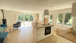 A modern kitchen with a central island, a dining area with a table and chairs, a blue sofa, and a stone fireplace.