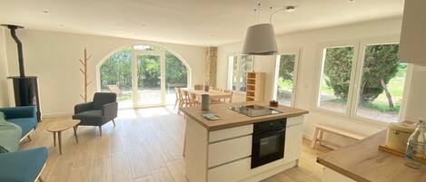 A modern kitchen with a central island, a dining area with a table and chairs, a blue sofa, and a stone fireplace.