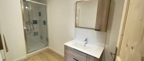 Un baño con cabina de ducha de vidrio, un lavabo blanco y un mueble de tocador de madera.