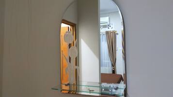 A mirror with a glass shelf, reflecting a room with a door and a curtain.
