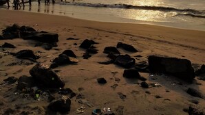 A beach with rocks and footprints, a group of people near the water, and the sun setting in the background. - Aqsa Guest House Ciamis (Ciamis)