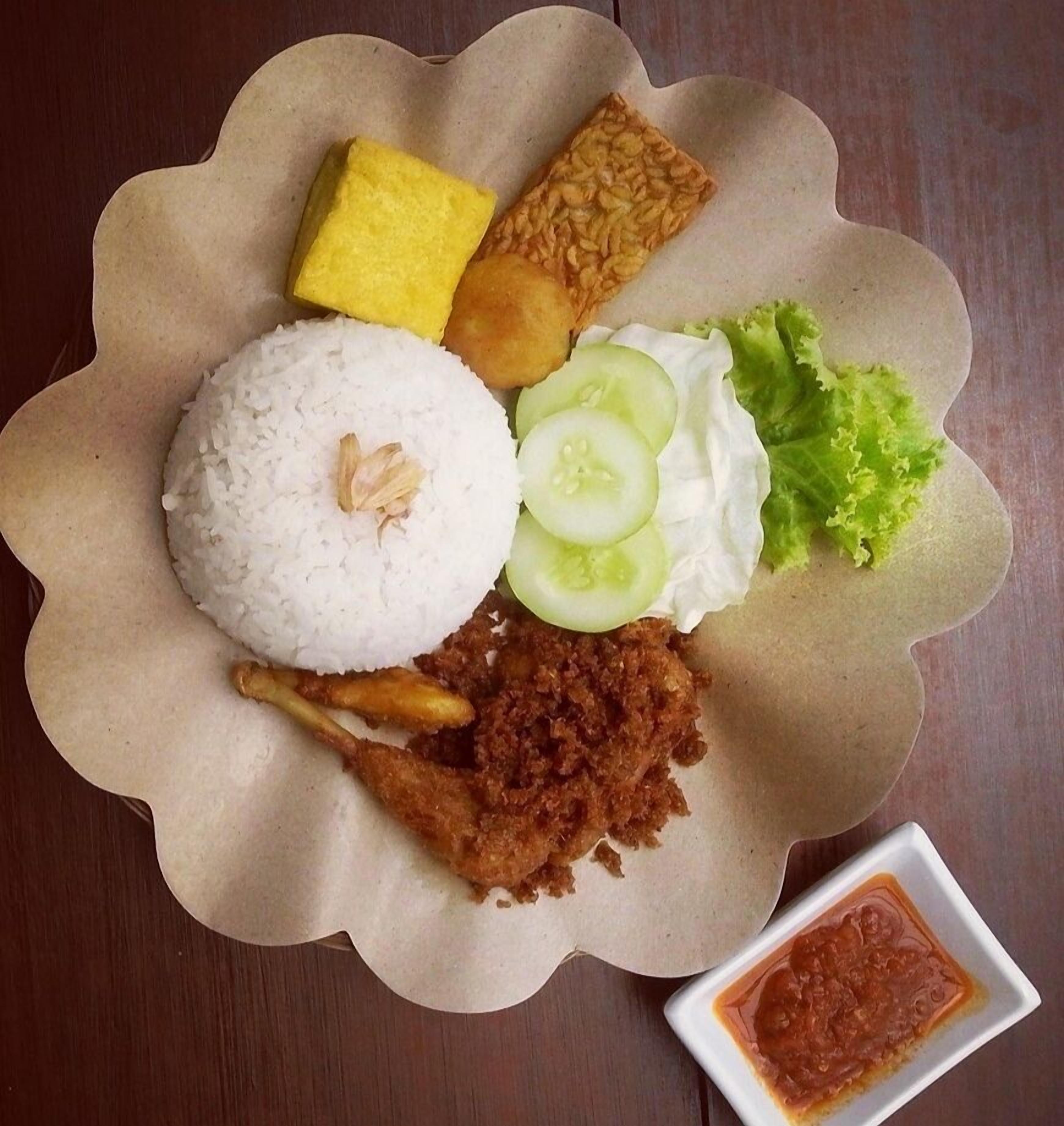 Une assiette de nourriture comprenant du riz, du poulet frit, des légumes et une portion de sauce à part.