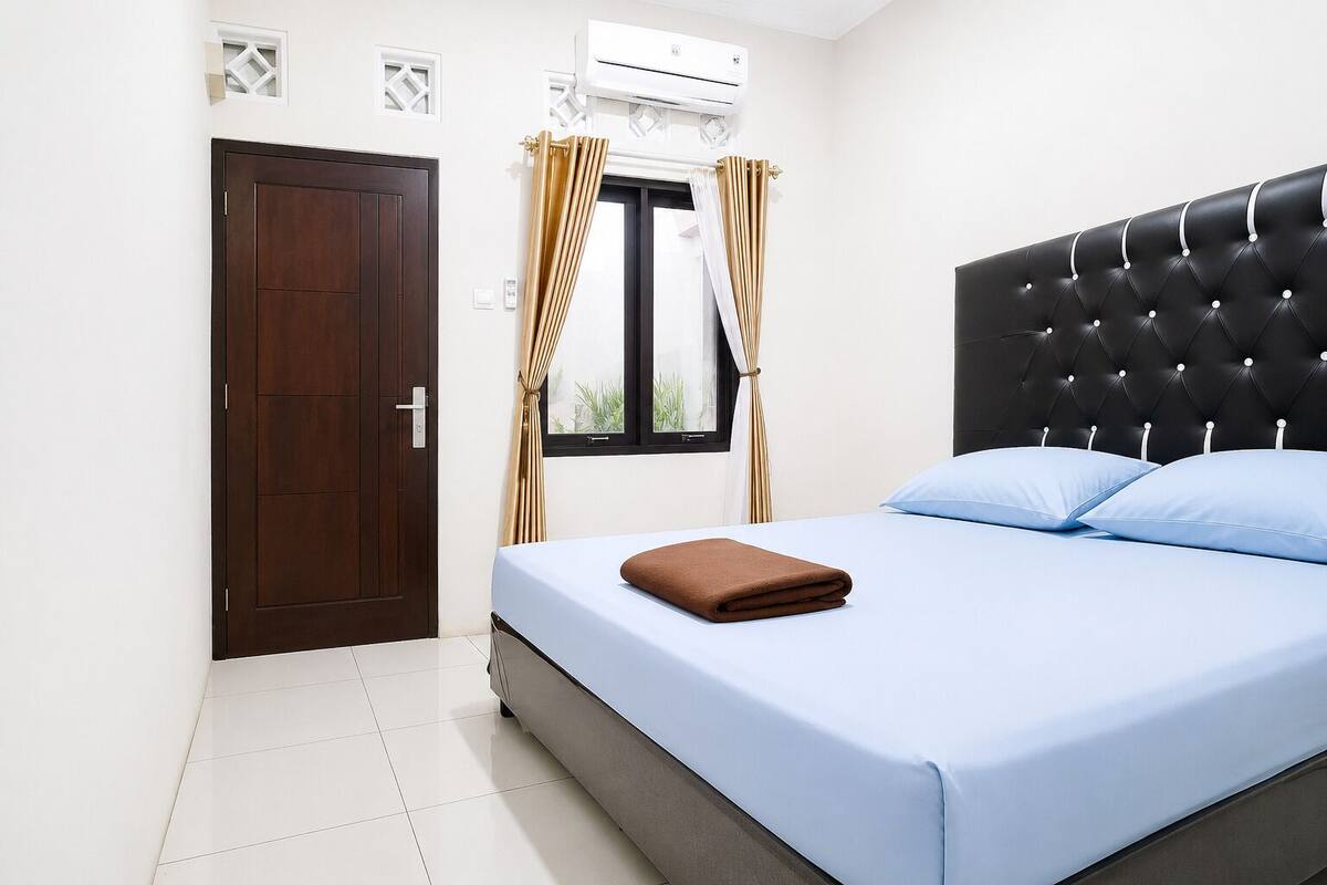 A bedroom with a bed, a window with curtains, a door, and an air conditioning unit.