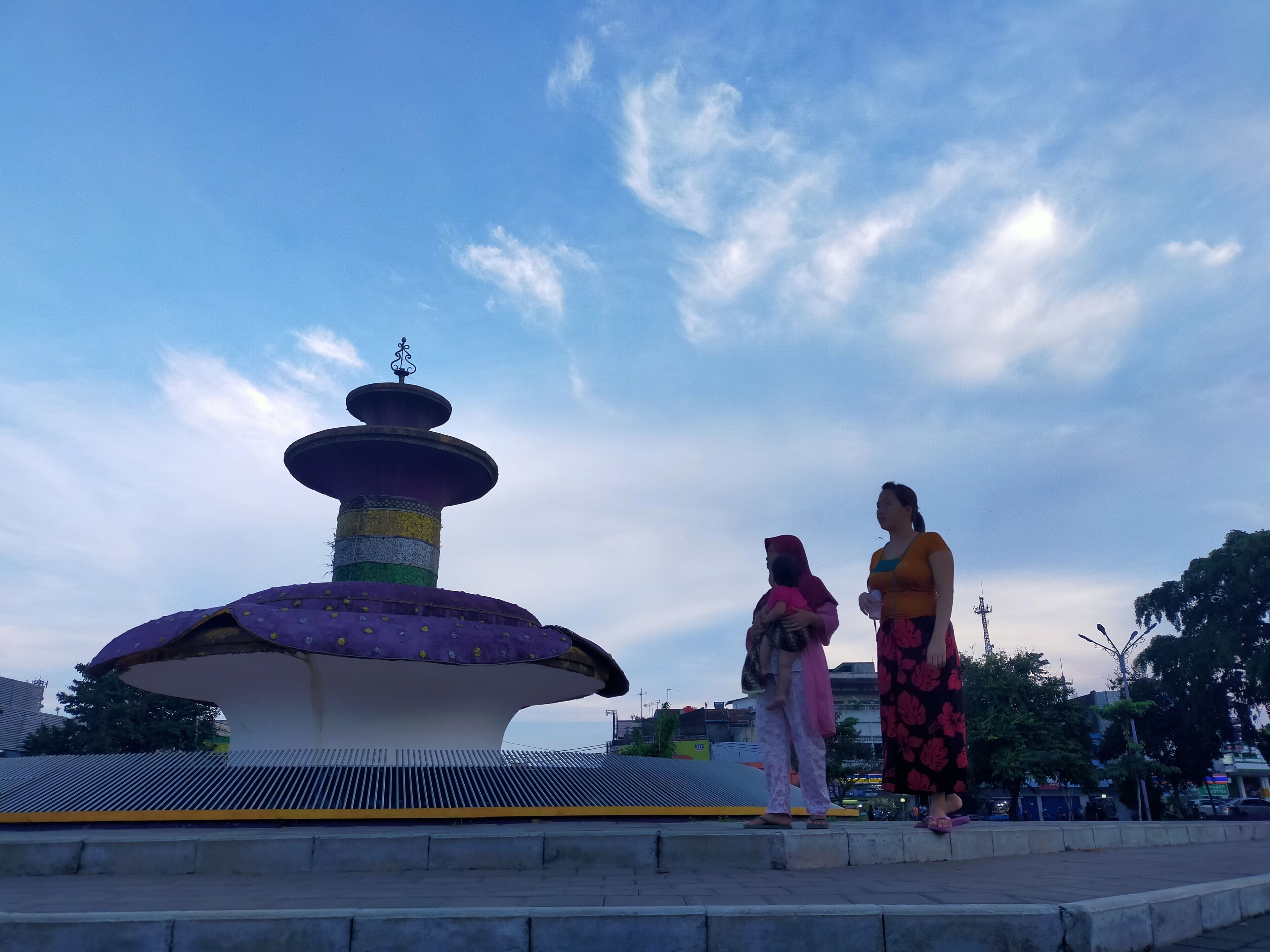 Une grande fontaine aux couleurs vives, à plusieurs niveaux, entourée d’une zone pavée avec des marches menant à sa base.