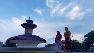 Une grande fontaine aux couleurs vives, à plusieurs niveaux, entourée d’une zone pavée avec des marches menant à sa base.