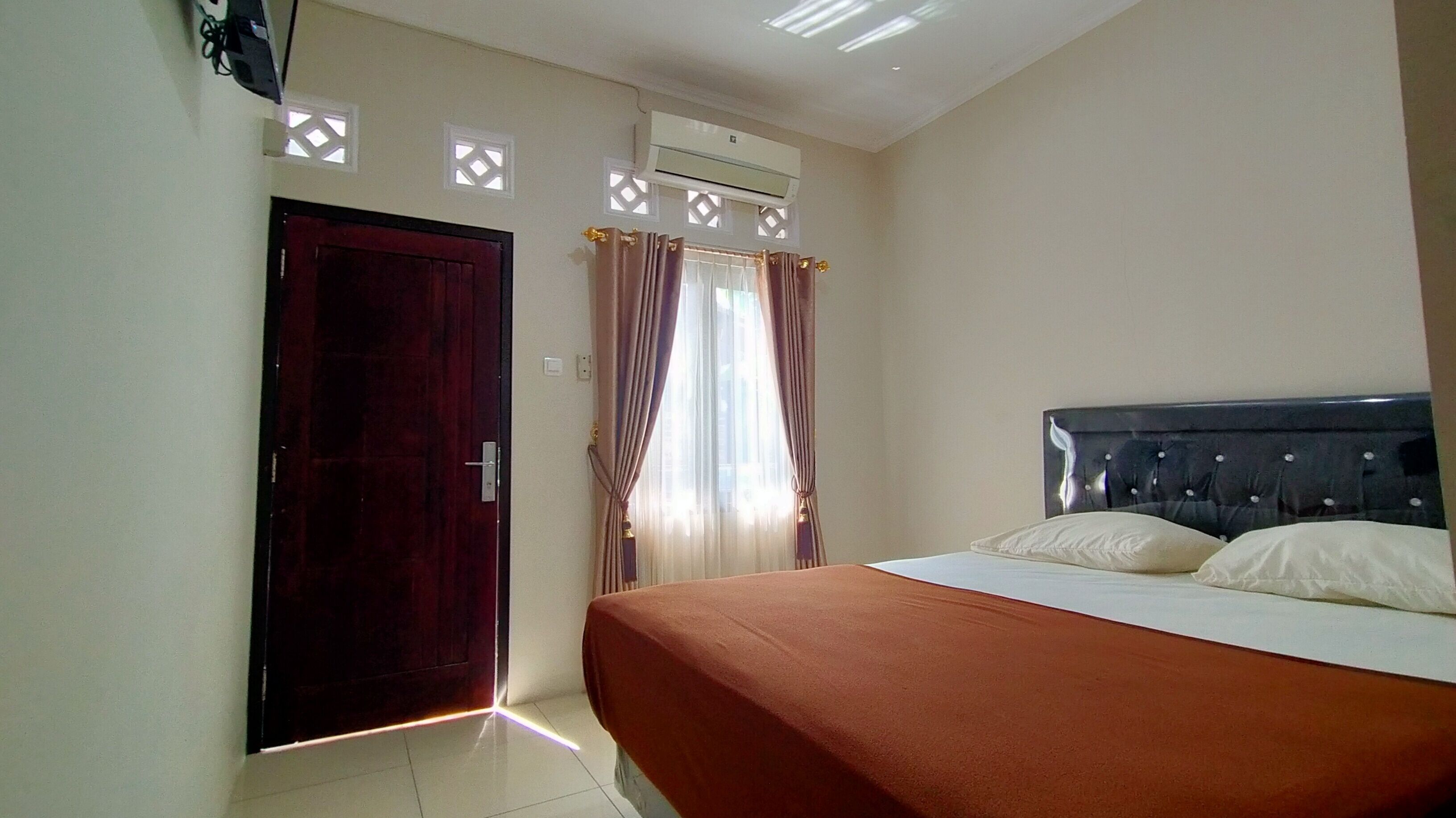 A bedroom with a bed, a door, an air conditioning unit, and a window with curtains.