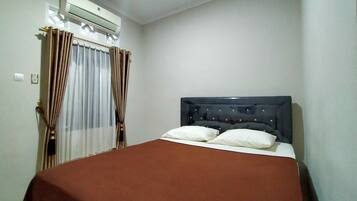 A single bed with a dark headboard and two pillows, a brown bedspread, and a window with curtains.