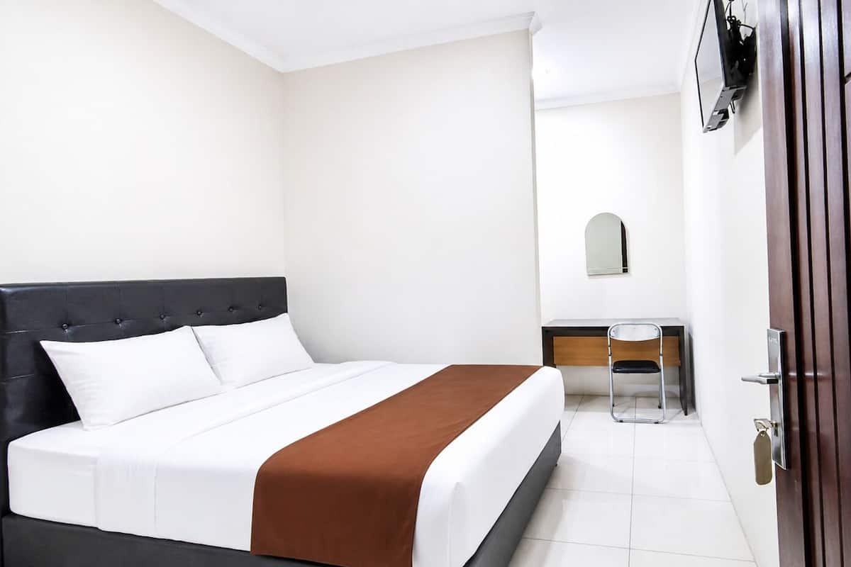 A hotel room with a bed, a desk, a chair, a wardrobe, and a mirror.