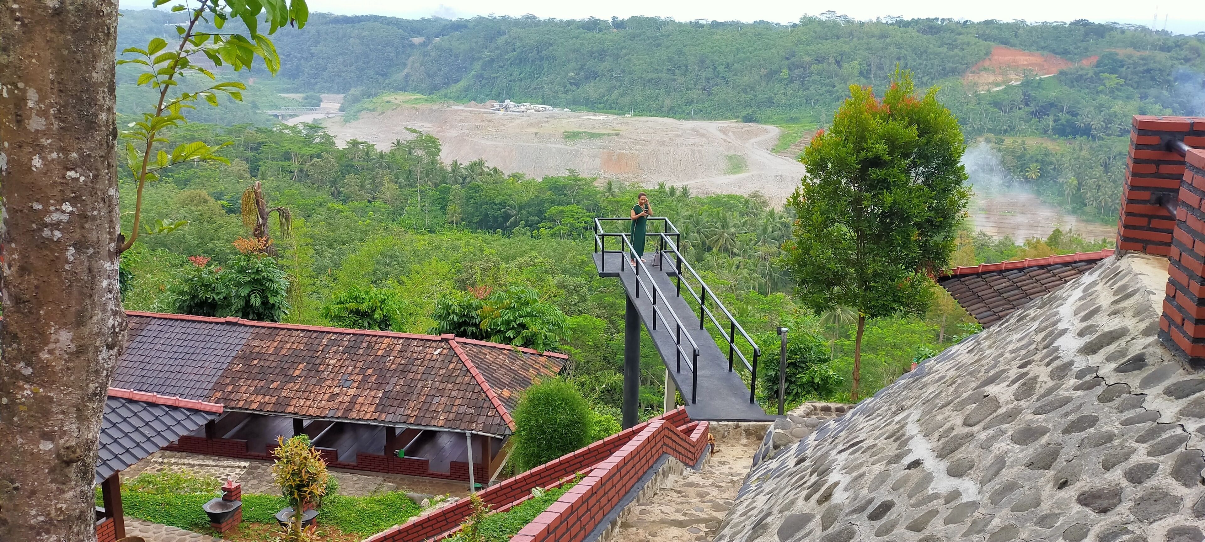 A view of a rural landscape with a staircase leading to a higher elevation, surrounded by greenery and a distant construction site.
