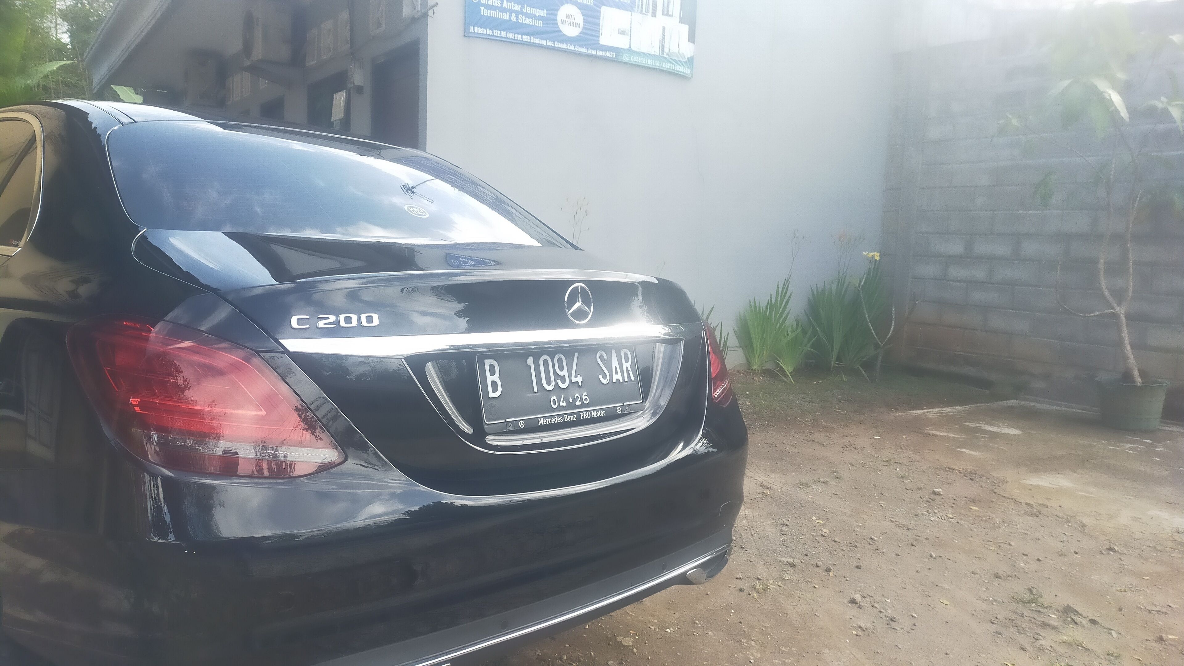 A black Mercedes-Benz C200 parked in front of a building with a sign that reads "Grats Antar Jemput Terminal & Stasion."